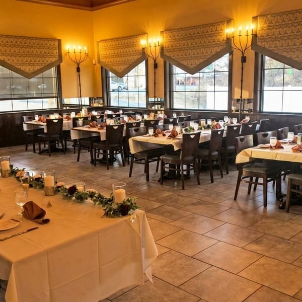 A restaurant dining room with multiple long tables set with white tablecloths, place settings, and floral centerpieces.