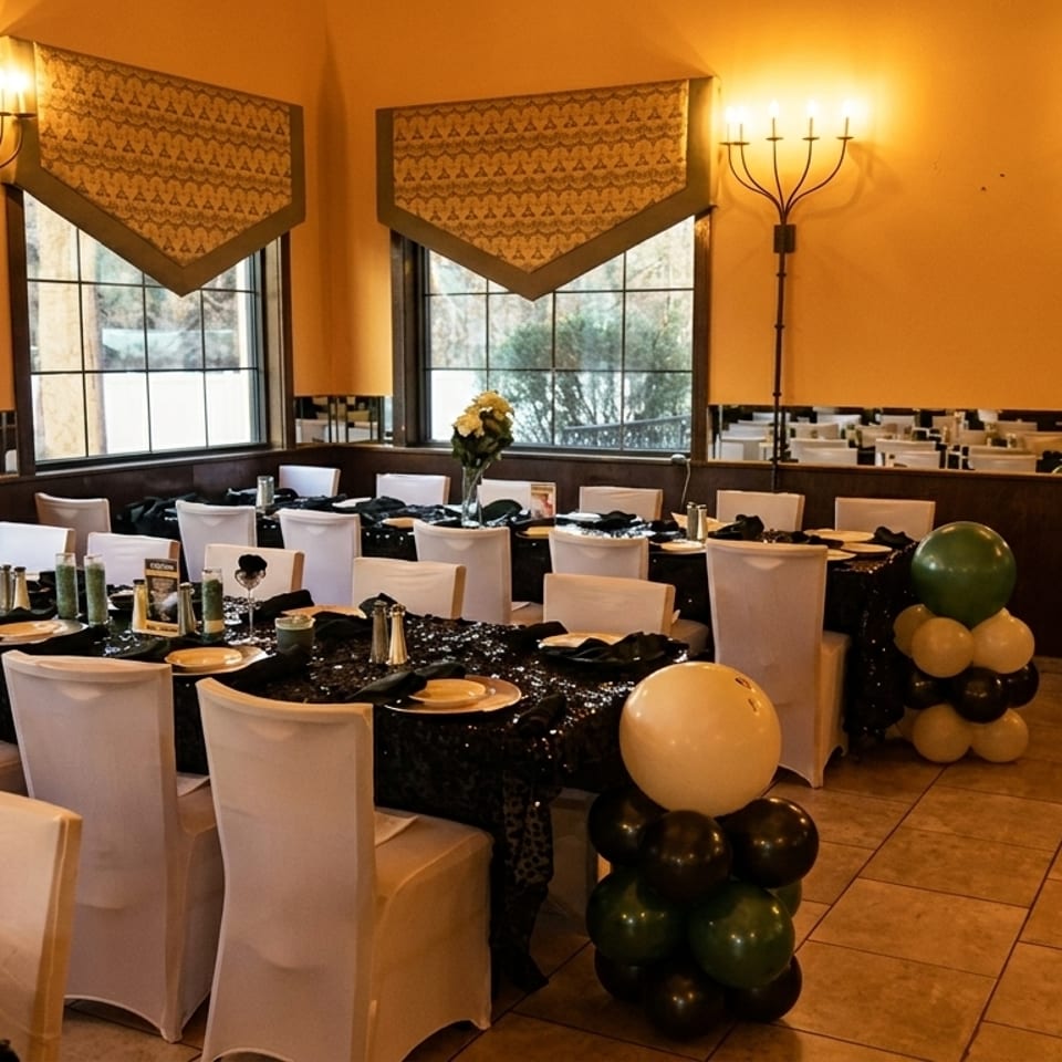 A restaurant dining room set for an event with black sequin tablecloths, white chairs, and balloon decorations.