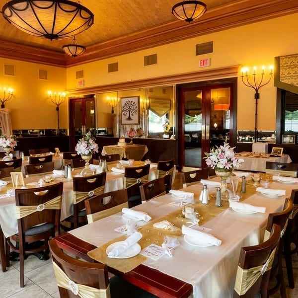 Elegant dining room with tables set for a special event, featuring floral centerpieces and warm lighting.