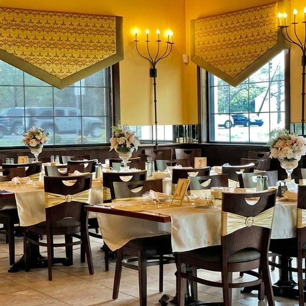 Elegant restaurant dining room with set tables, floral centerpieces, and candelabra wall sconces.