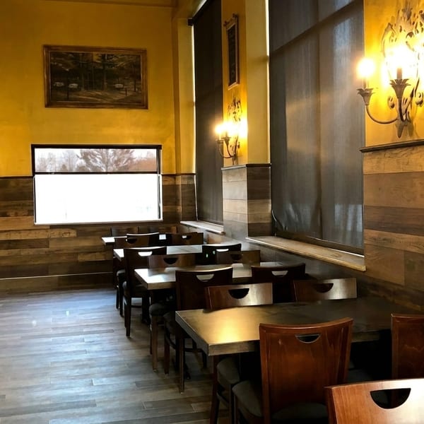 Empty restaurant dining room with yellow walls, wood paneling, dark tables, and chairs.