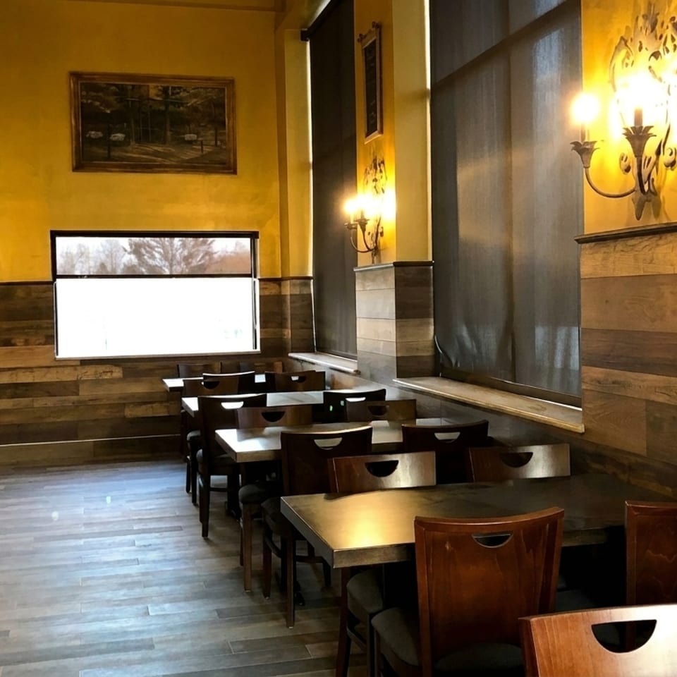 Empty restaurant dining room with yellow walls, wood paneling, dark tables, and chairs.