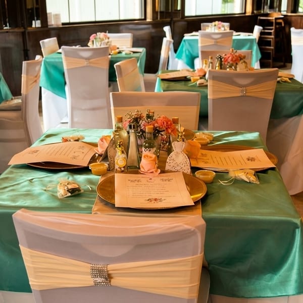 Restaurant dining room set with teal tablecloths, white chair covers, and floral centerpieces.