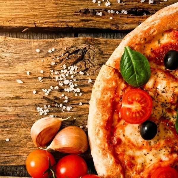 Half a pizza with tomatoes, olives, and basil on a rustic wooden table with garlic.