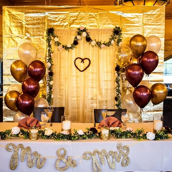 A decorated "Mr. & Mrs." table with balloons, flowers, and candles against a gold backdrop.